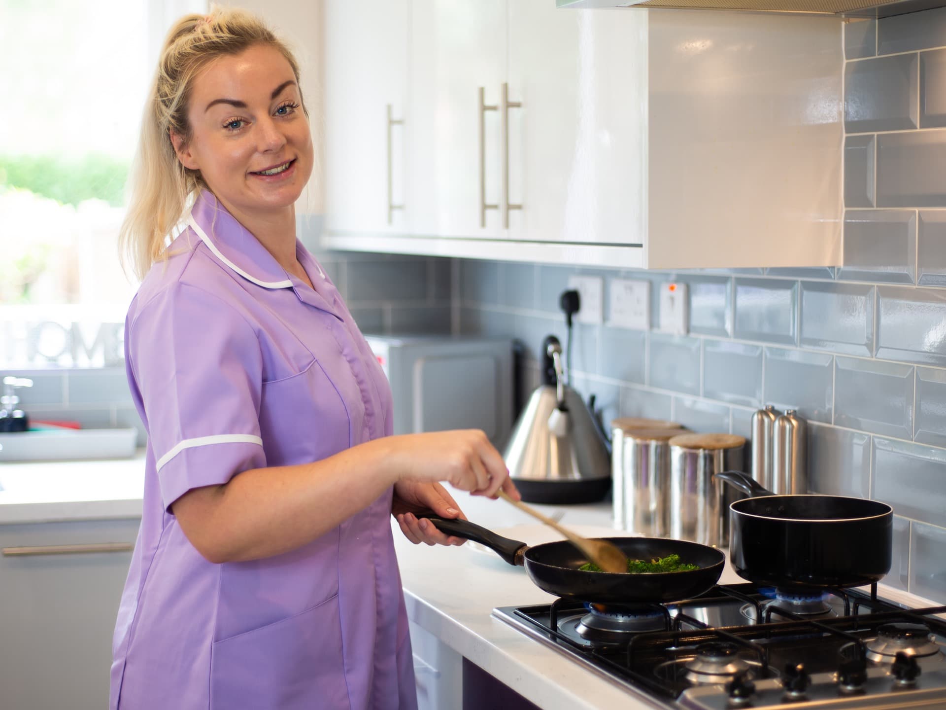 Female carer cooking using gas cooker kitchen kettle saucepans