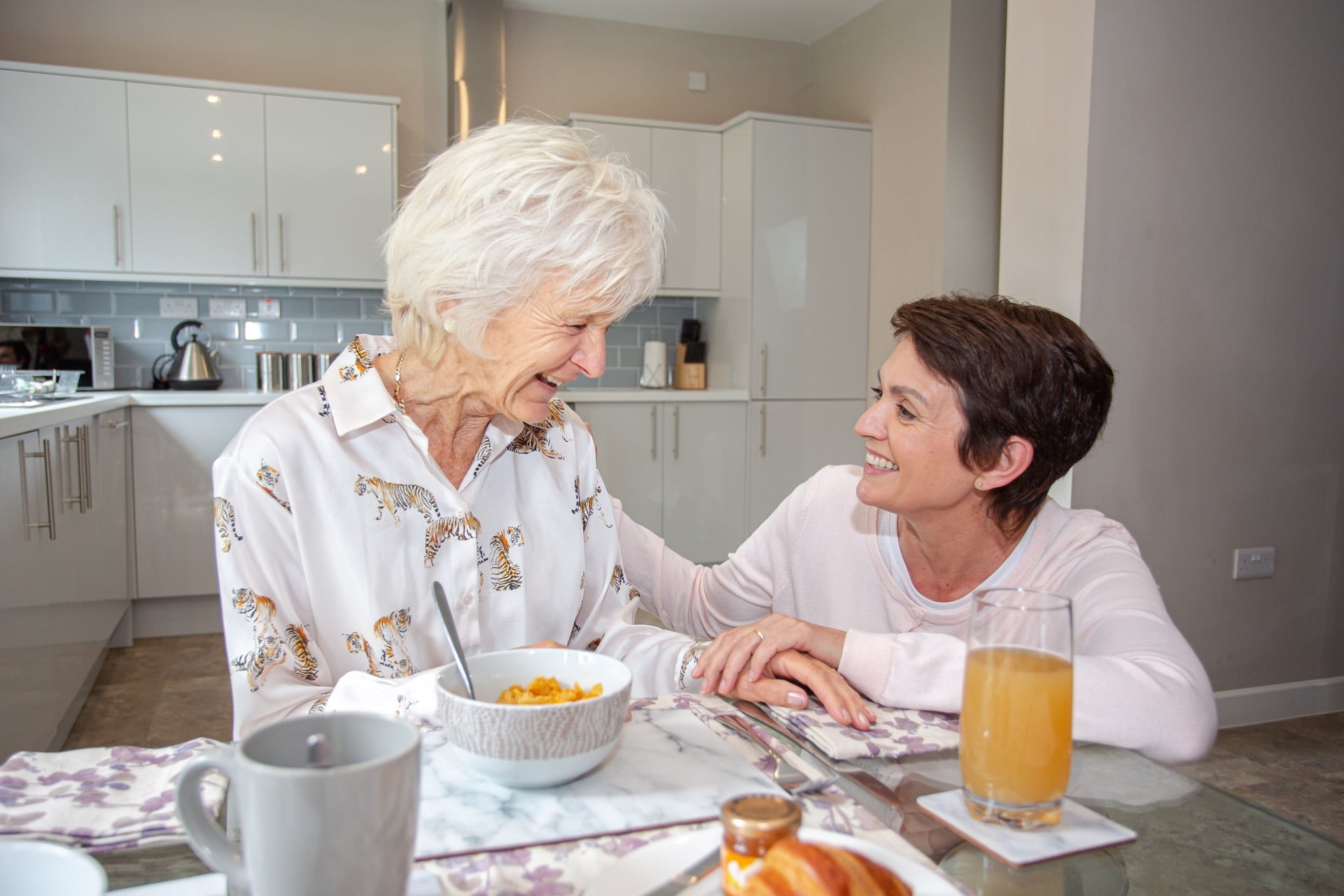 female personal carer crouching beside elderly lady having breakfast