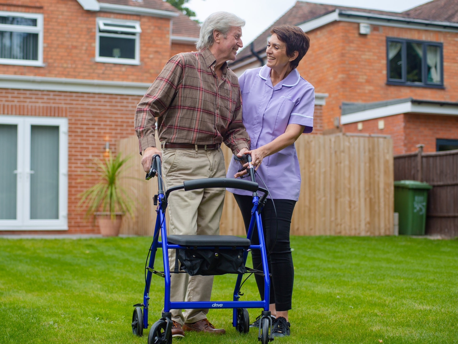 female dementia care assistant helping elderly man to use a walker